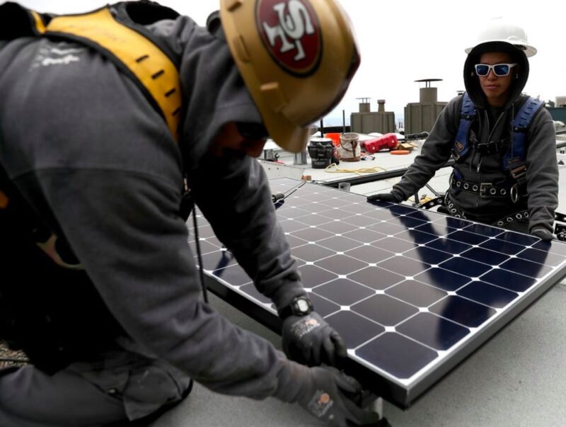 Two workers installing solar panels on a flat roof.