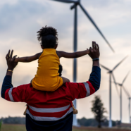 Child rides joyfully on dad's shoulders with windmills in the background.